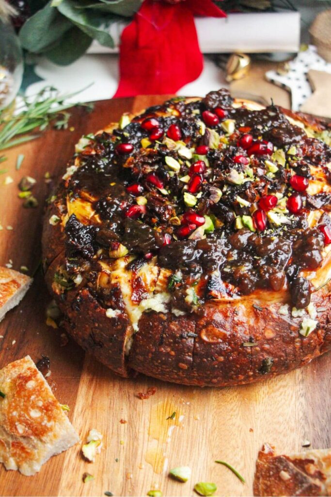 Baked brie in a loaf of bread, topped with fig jam and pomegranate seeds.