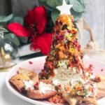 Coated Christmas tree cheese ball topped with a cheese star on a pink plate with pita chips on the side.