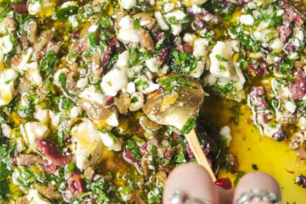 Hand mixing ingredients for Greek dipping oil in a large white plate.