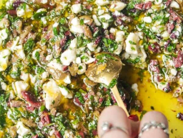 Hand mixing ingredients for Greek dipping oil in a large white plate.