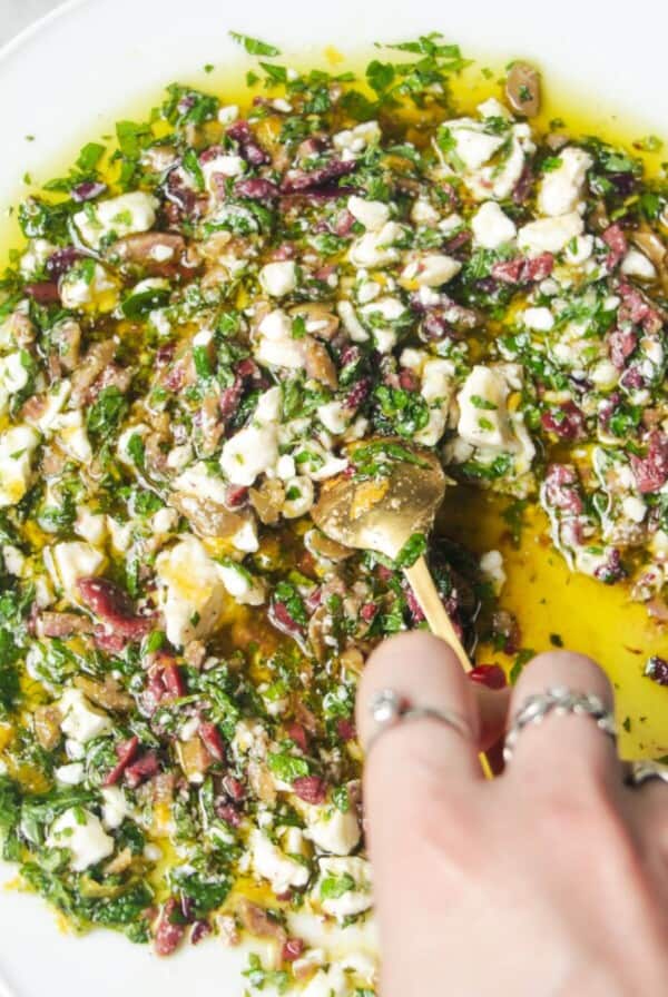 Hand mixing ingredients for Greek dipping oil in a large white plate.