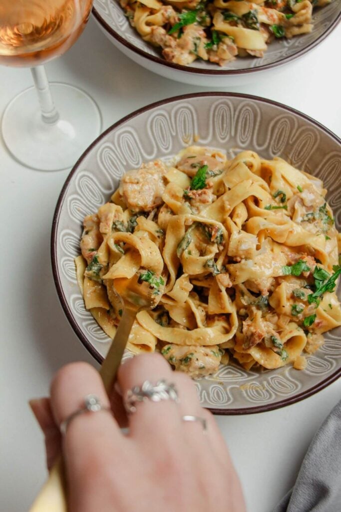 Hand twirling fork through a bowl of colourful fettuccine.