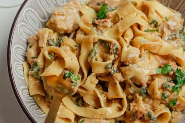 Hand twirling fork through a bowl of colourful fettuccine.