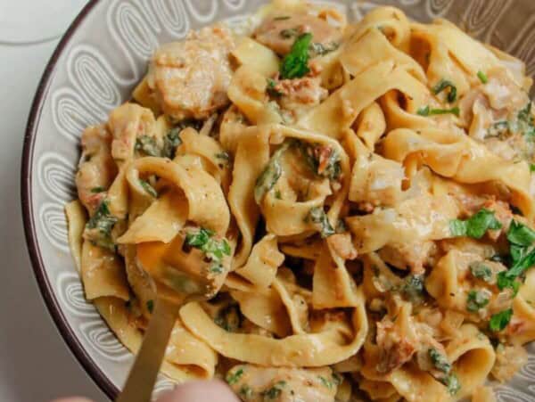 Hand twirling fork through a bowl of colourful fettuccine.