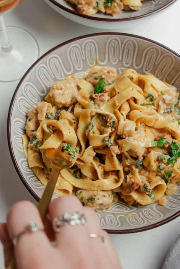 Hand twirling fork through a bowl of colourful fettuccine.