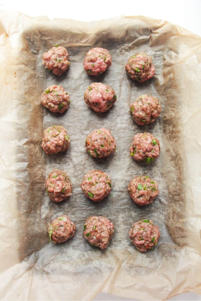 Rolled meatballs on a lined oven tray.