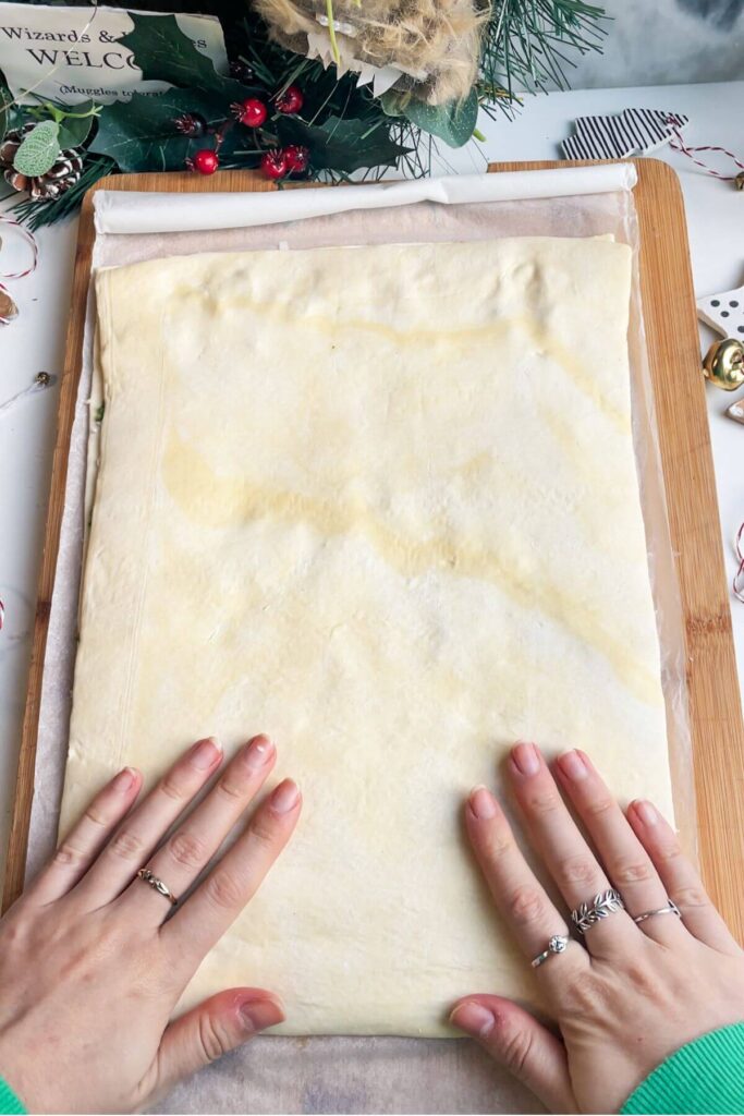 Flattening puff pastry on a wooden board.