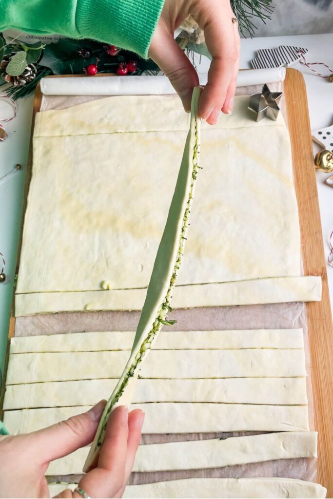 Holding up a strip of puff pastry layered with basil pesto and mozzarella.