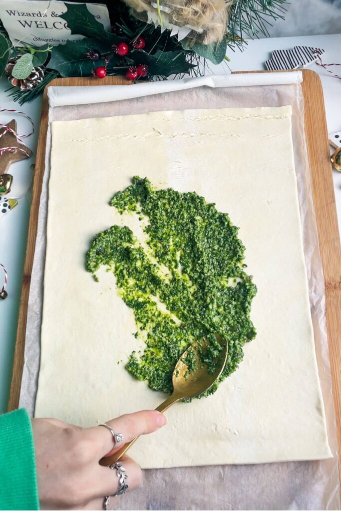 Spooning basil pesto onto a sheet of puff pastry.