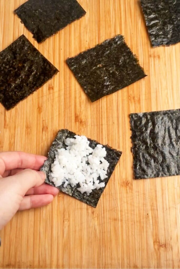 Hand holding a piece of nori with sushi rice on it.