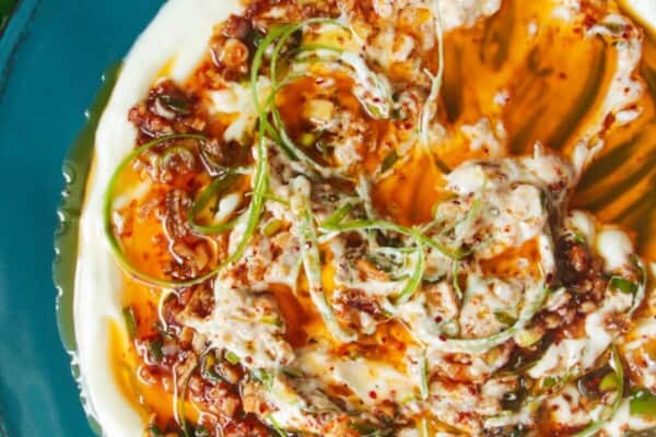 Sizzling oil on top of creamy Greek yogurt on a teal plate.