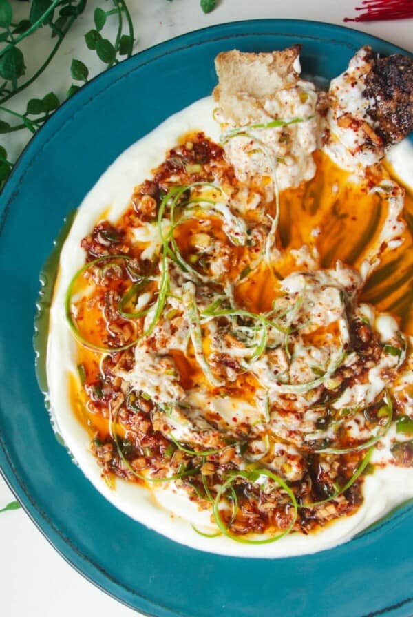 Sizzling oil on top of creamy Greek yogurt on a teal plate.