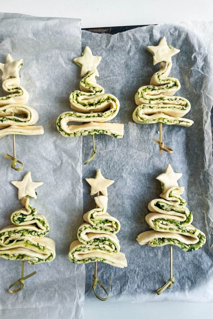 Six unbaked pesto Christmas tree on a lined oven tray.