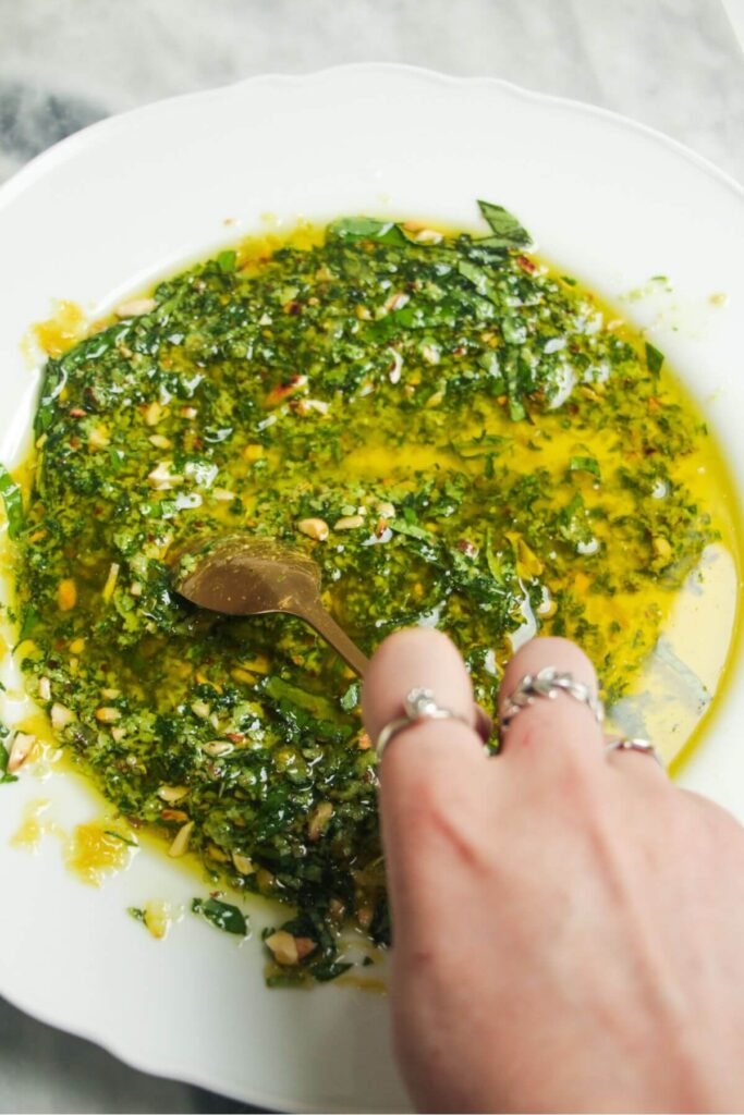 Hand holding spoon, mixing pesto dipping oil on a plate.