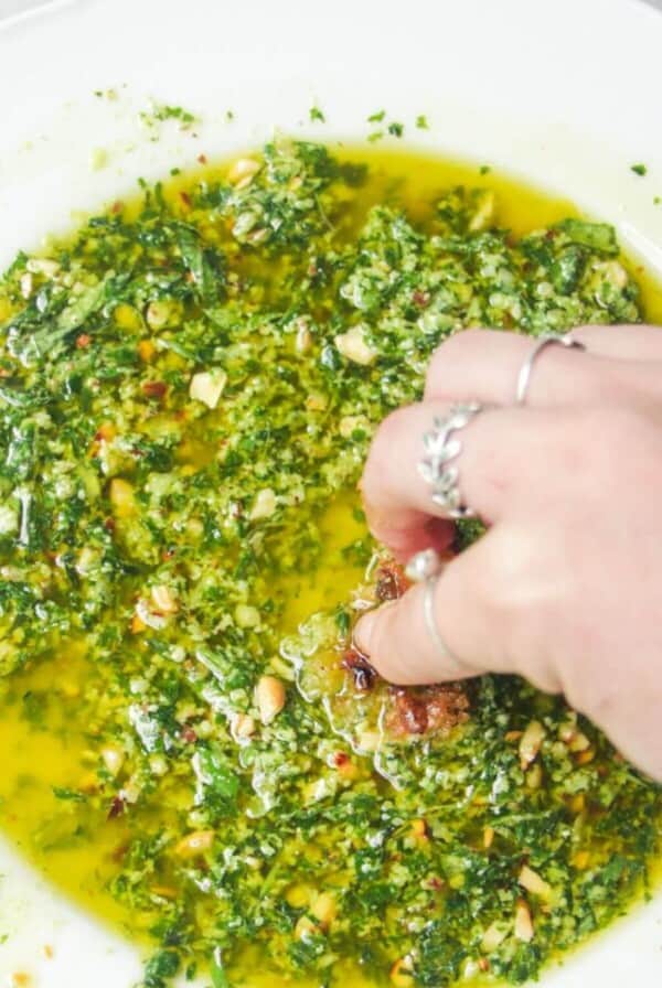 A hand sweeping bread through pesto dipping oil in a scalloped white plate.