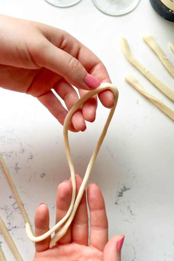 Hands holding up a strand of pici pasta.