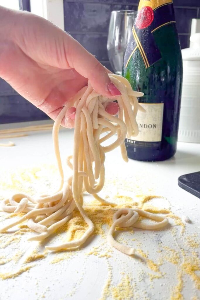 Hand tossing pici strands with a bottle of champagne in the background.