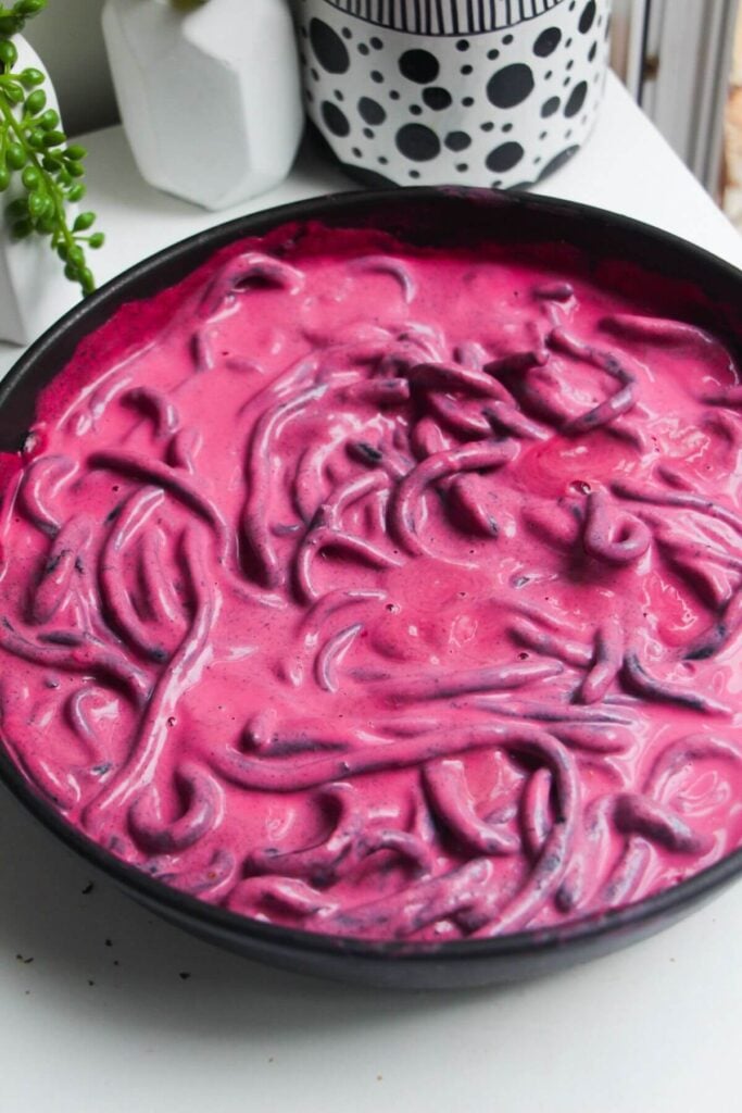 Squid ink pici mixed through pink beet pasta sauce in a pan.