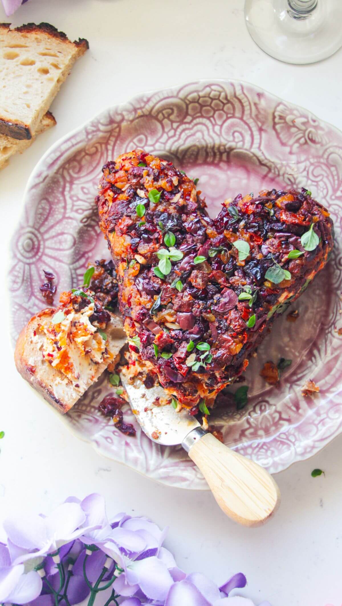 Heart shaped cheese ball, covered in dried fruit on a small pink plate, with bread on the side.