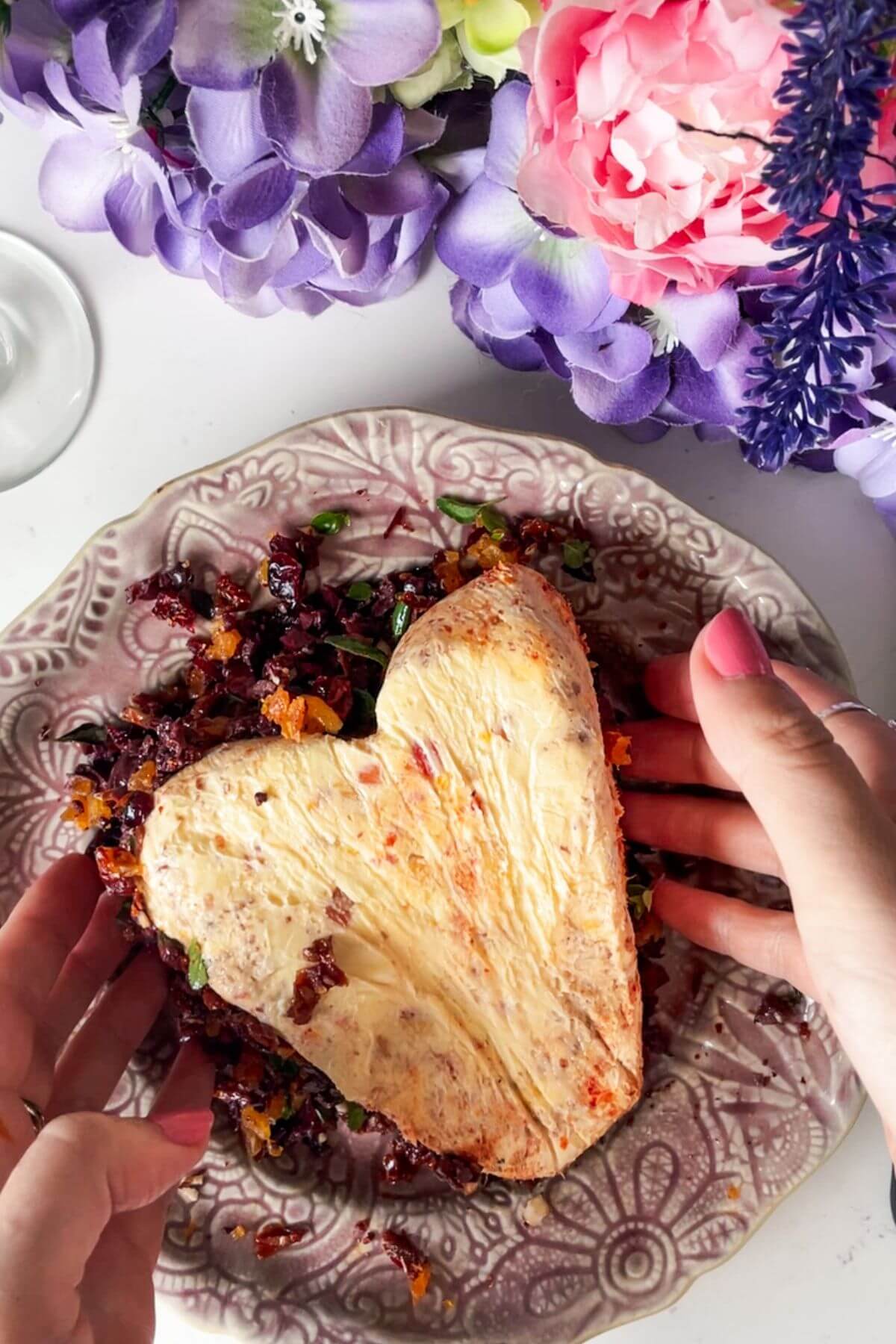 Hands pressing topping into the sides of the cheese heart on a small plate.