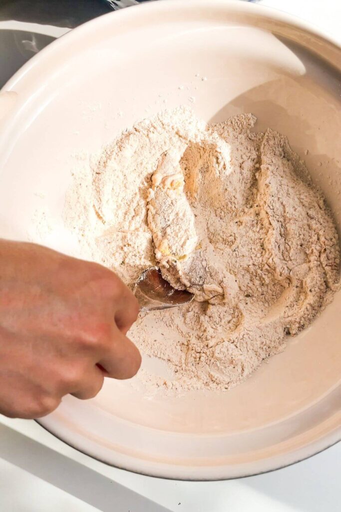 Mixing marinated chicken tender with flour coating in a mixing bowl.