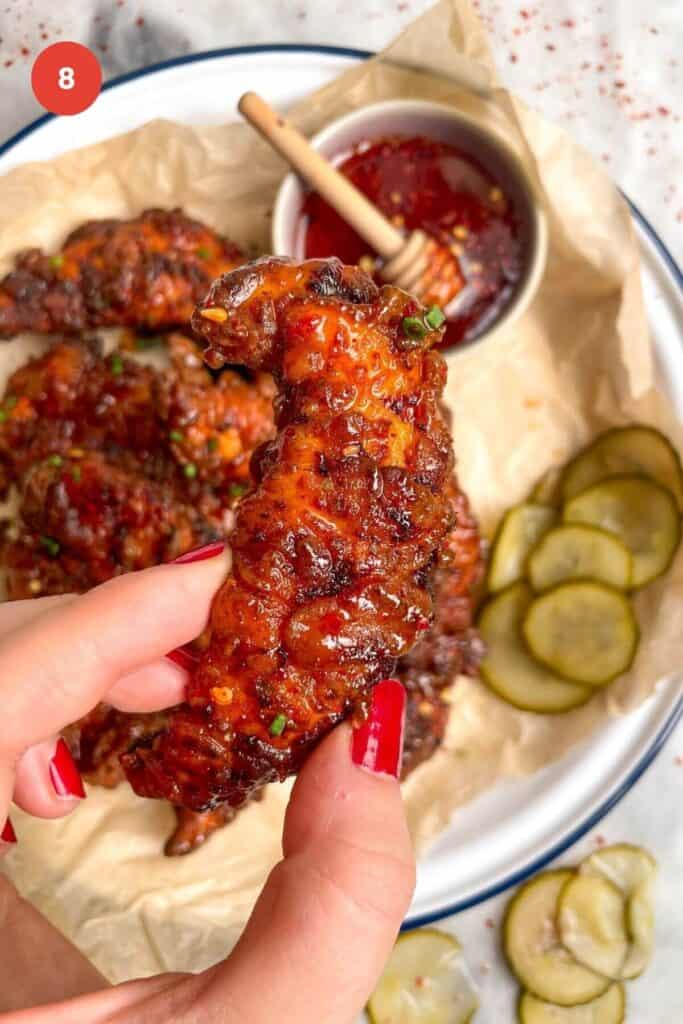 Hand holding a fried chicken tender with more tenders in the background.