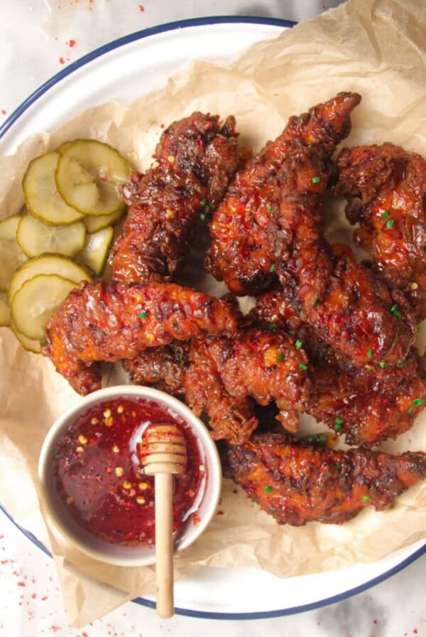 Plate of crispy hot honey chicken tenders with hot honey sauce on the side.
