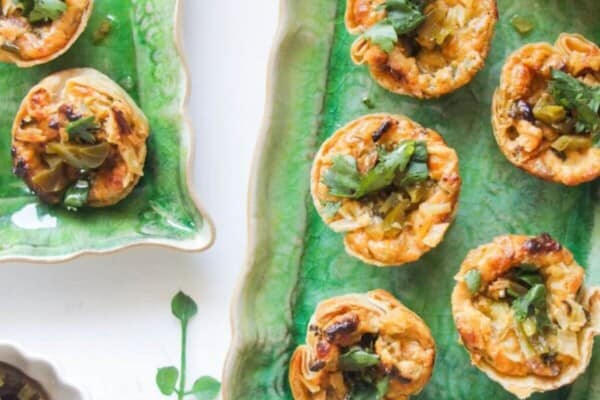 Jalapeno popper taco cups on a green rectangular plate, with a bowl of jalapenos on the side.