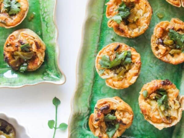 Jalapeno popper taco cups on a green rectangular plate, with a bowl of jalapenos on the side.