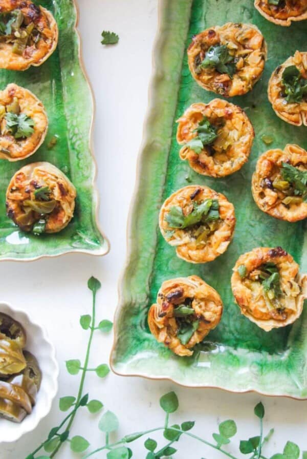 Jalapeno popper taco cups on a green rectangular plate, with a bowl of jalapenos on the side.