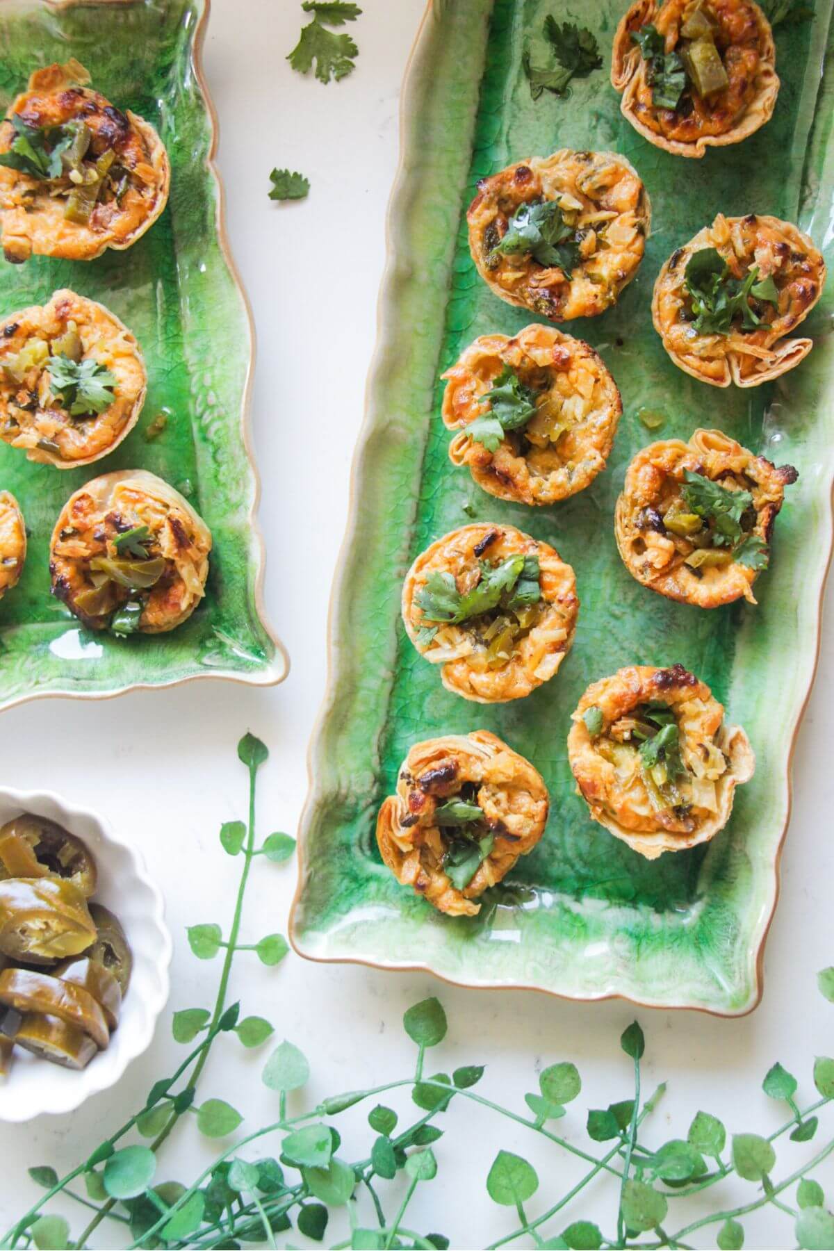 Jalapeno popper taco cups on a green rectangular plate, with a bowl of jalapenos on the side.