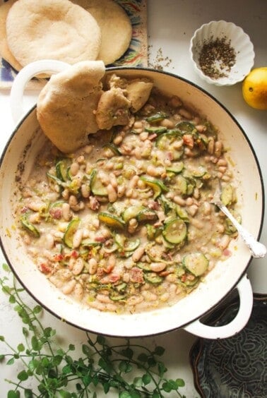 Creamy leek zucchini beans in a large pot with a silver spoon and pita bread on the side.