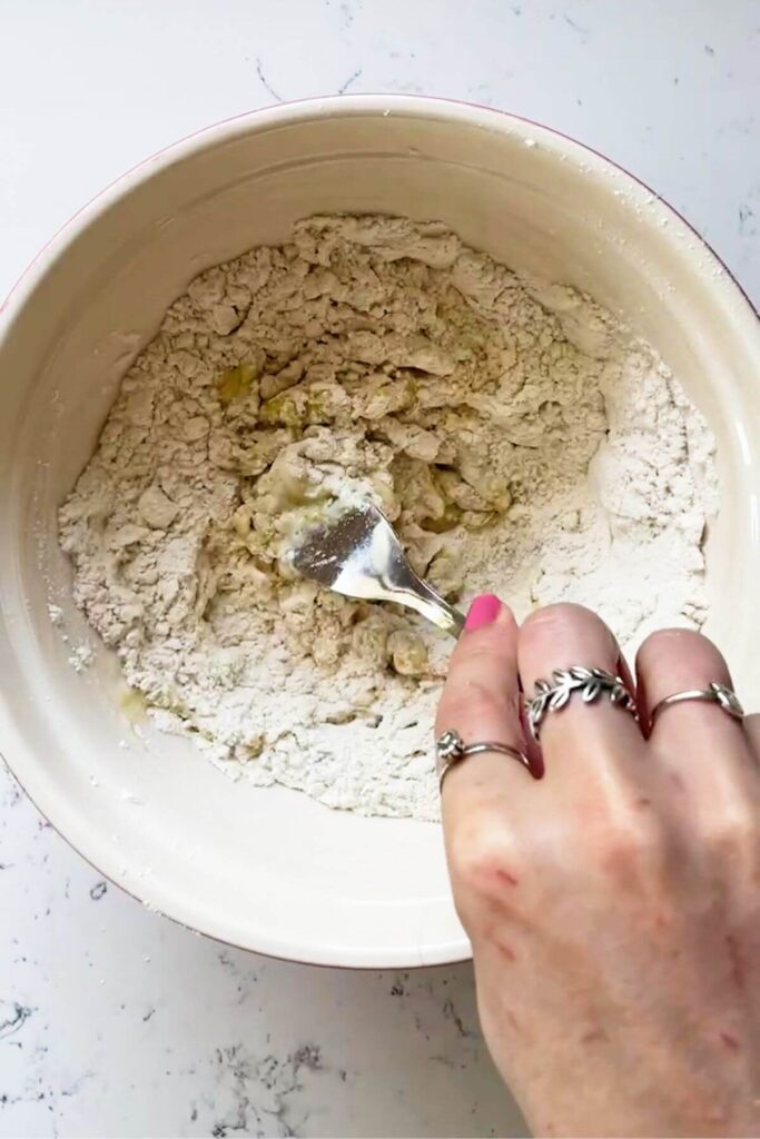 Hand holding a fork mixing flour, water and olive oil in a mixing bowl.