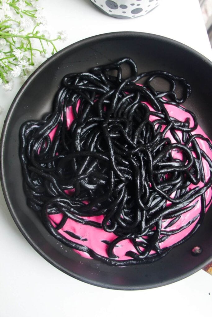 Squid ink pici in pink beet pasta sauce in a pan.