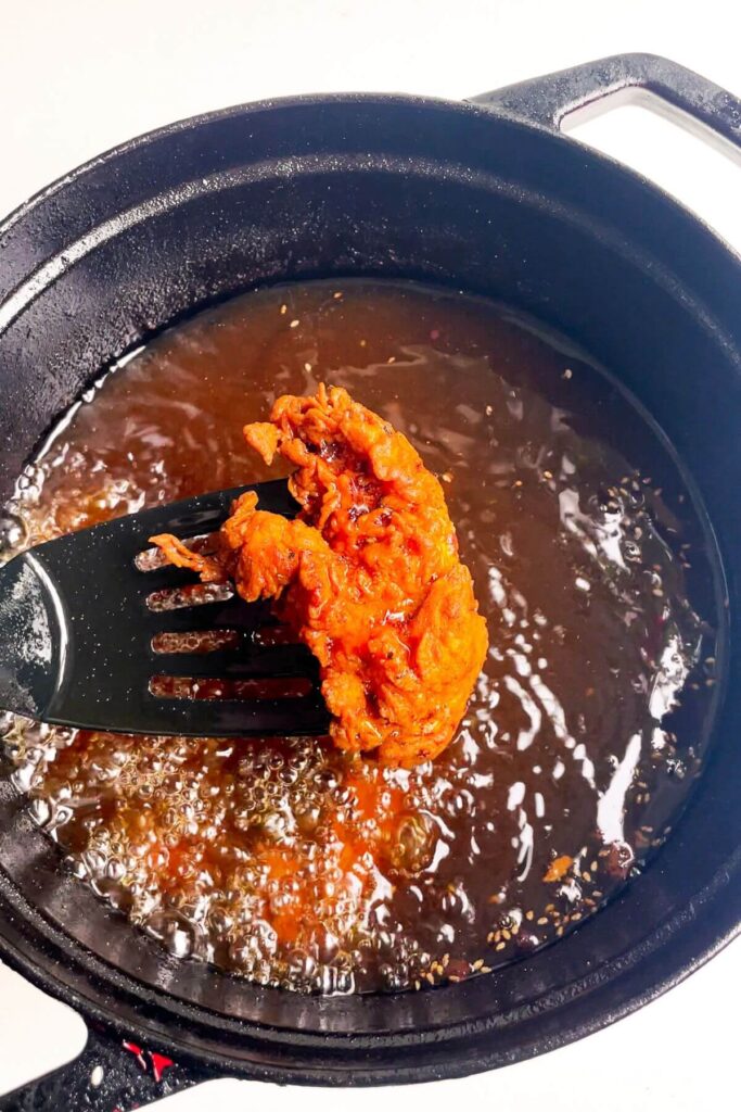 Fried chicken tender on a fish slice with pot of oil in the background.