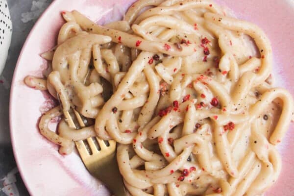 Cacio e pepe on a pink plate with gold fork in it.