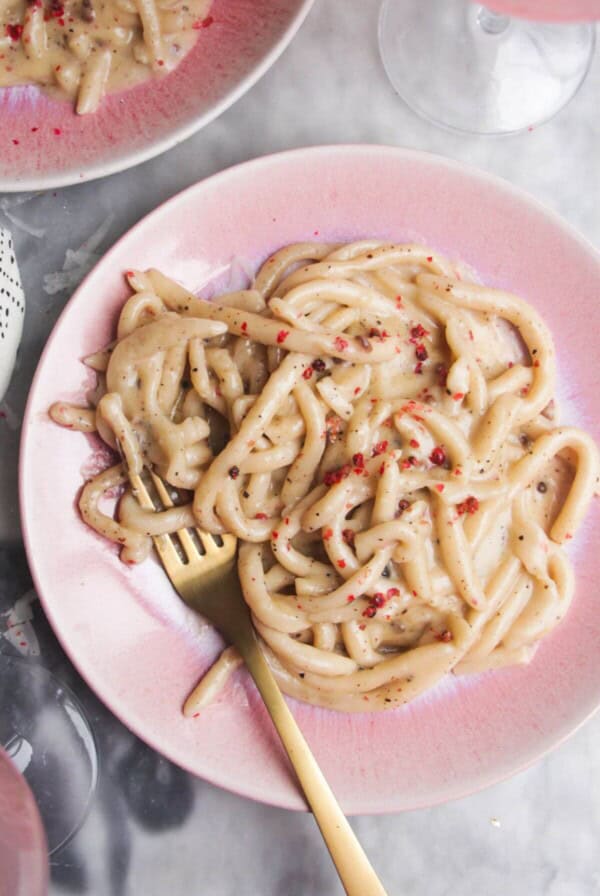 Cacio e pepe on a pink plate with gold fork in it.