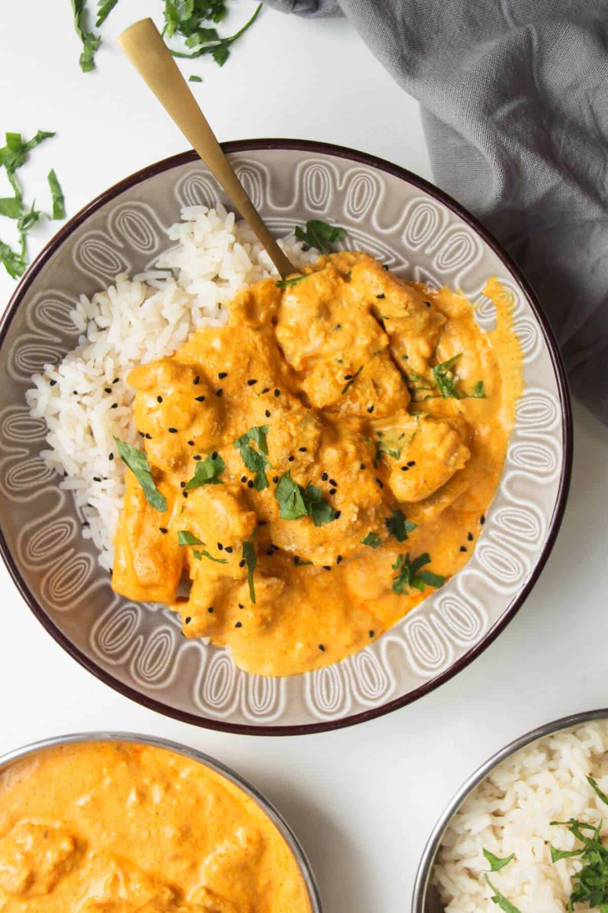 Chicken korma curry on top of rice in a bowl, with more curry and rice on the side.