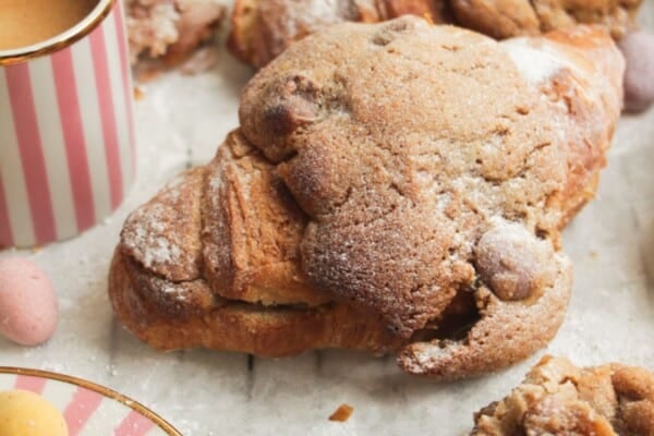 Cookie dough stuffed croissants on a lined baking tray with a coffee cup on the side.