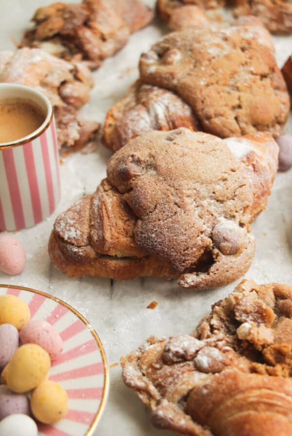 Cookie dough stuffed croissants on a lined baking tray with a coffee cup on the side.