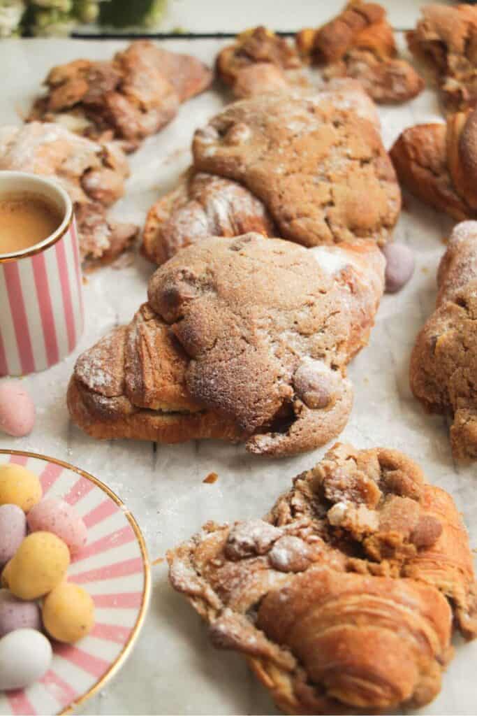 Cookie dough stuffed croissants on a lined baking tray with a coffee cup on the side.