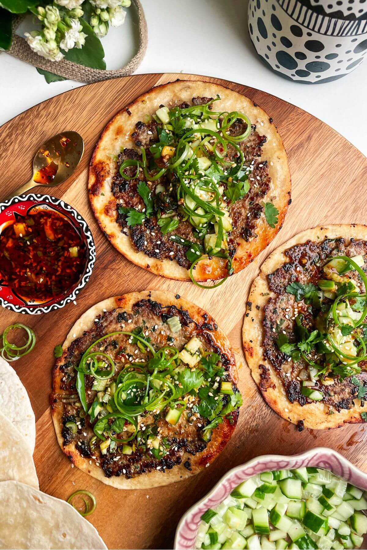 Three dumpling tacos on a wooden board with chilli oil on the side.