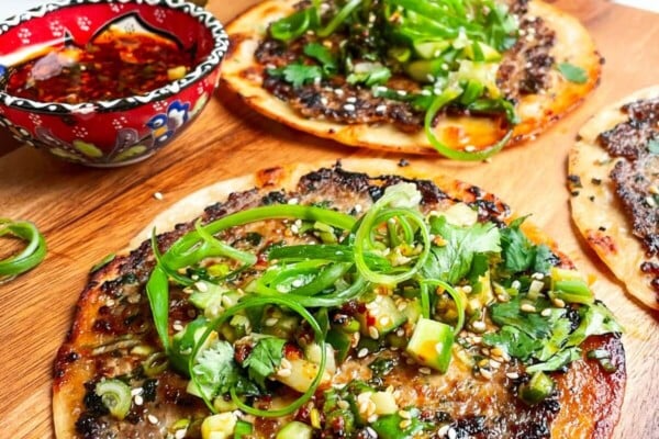 Three dumpling tacos on a wooden board with chilli oil on the side.