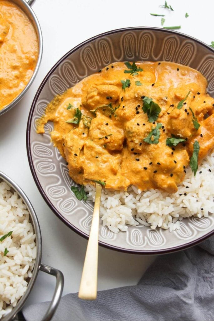 Chicken korma in a bowl over rice, with more curry on the side.