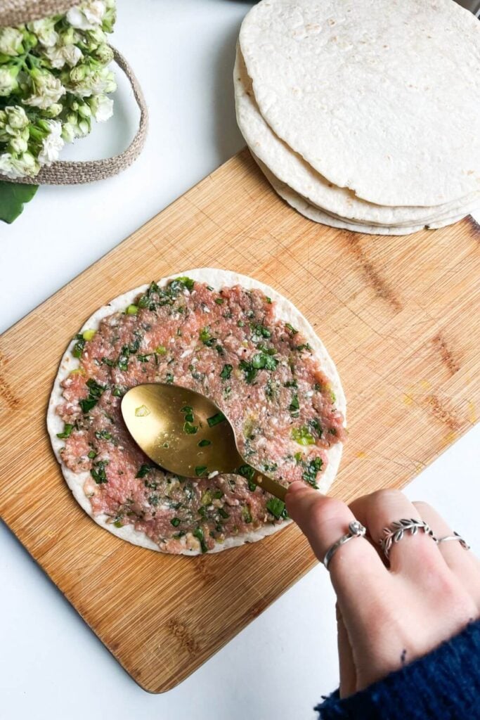 Hand holding a spoon, smoothing dumpling mixture onto a mini tortilla.