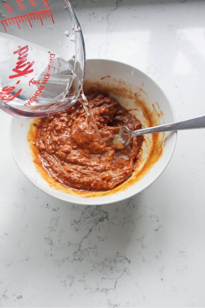 Pouring water into peanut sauce in a small bowl.