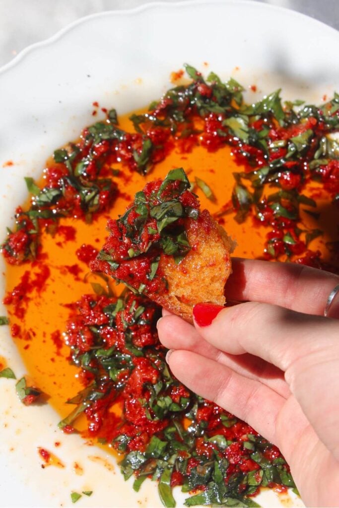 Hand holding up piece of bread with pizza dipping oil on it.