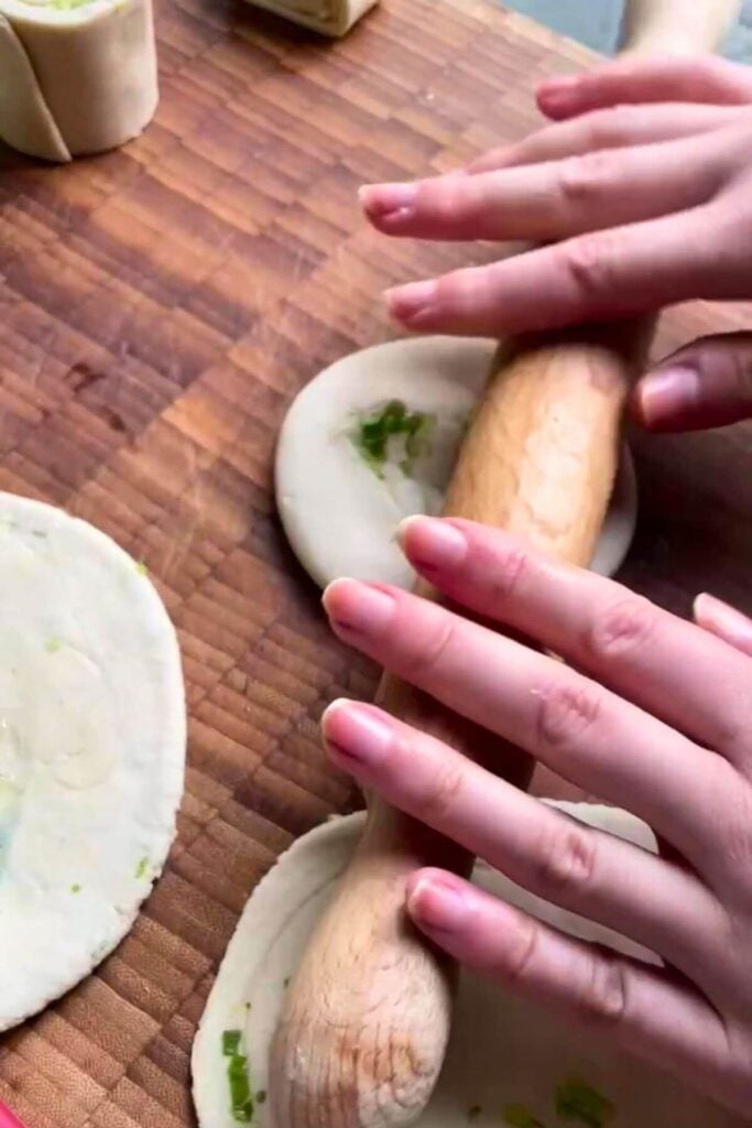 Rolling out scallion pancakes on a wooden board.