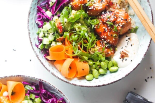 Two baked salmon poke bowls on a marble background with honey on the side.