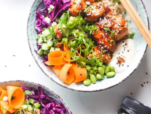 Two baked salmon poke bowls on a marble background with honey on the side.